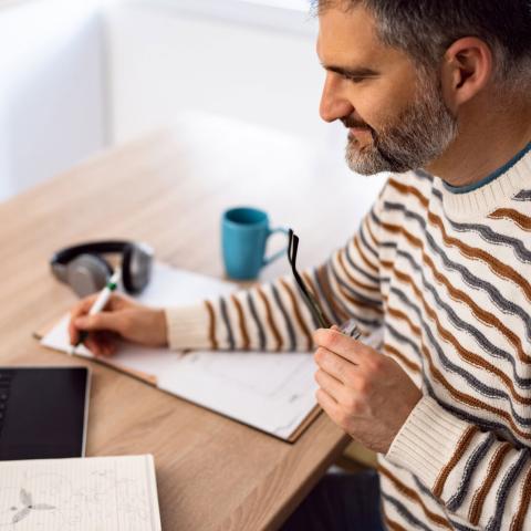 Man holding glasses writing on a pad