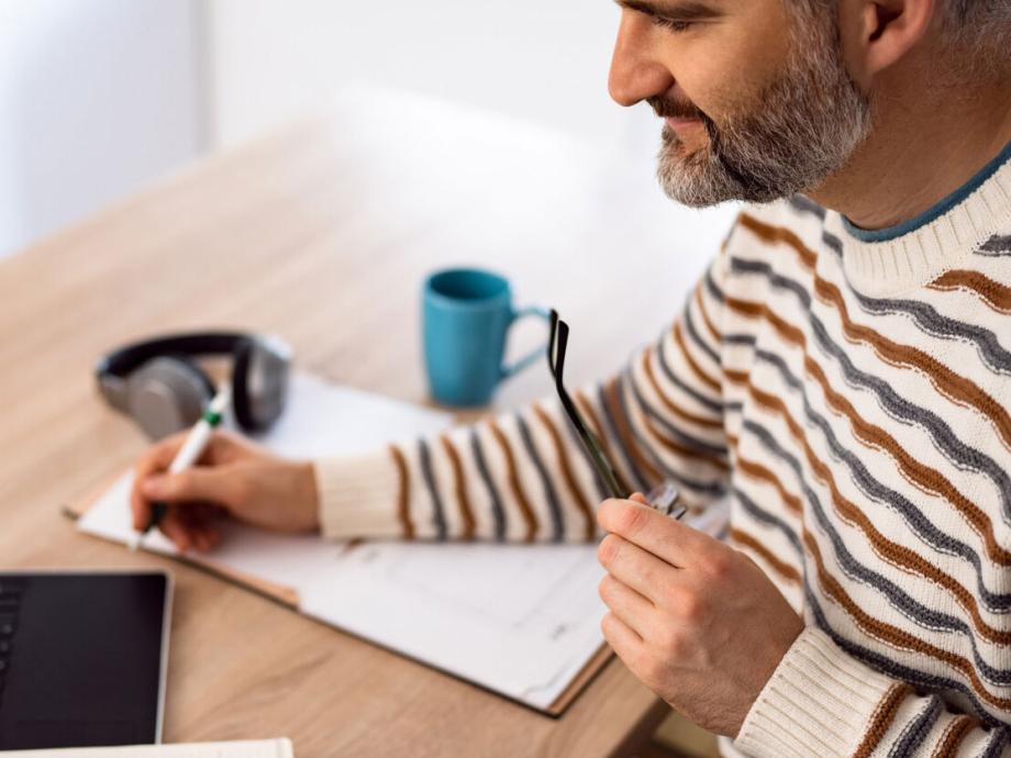 Man holding glasses writing on a pad